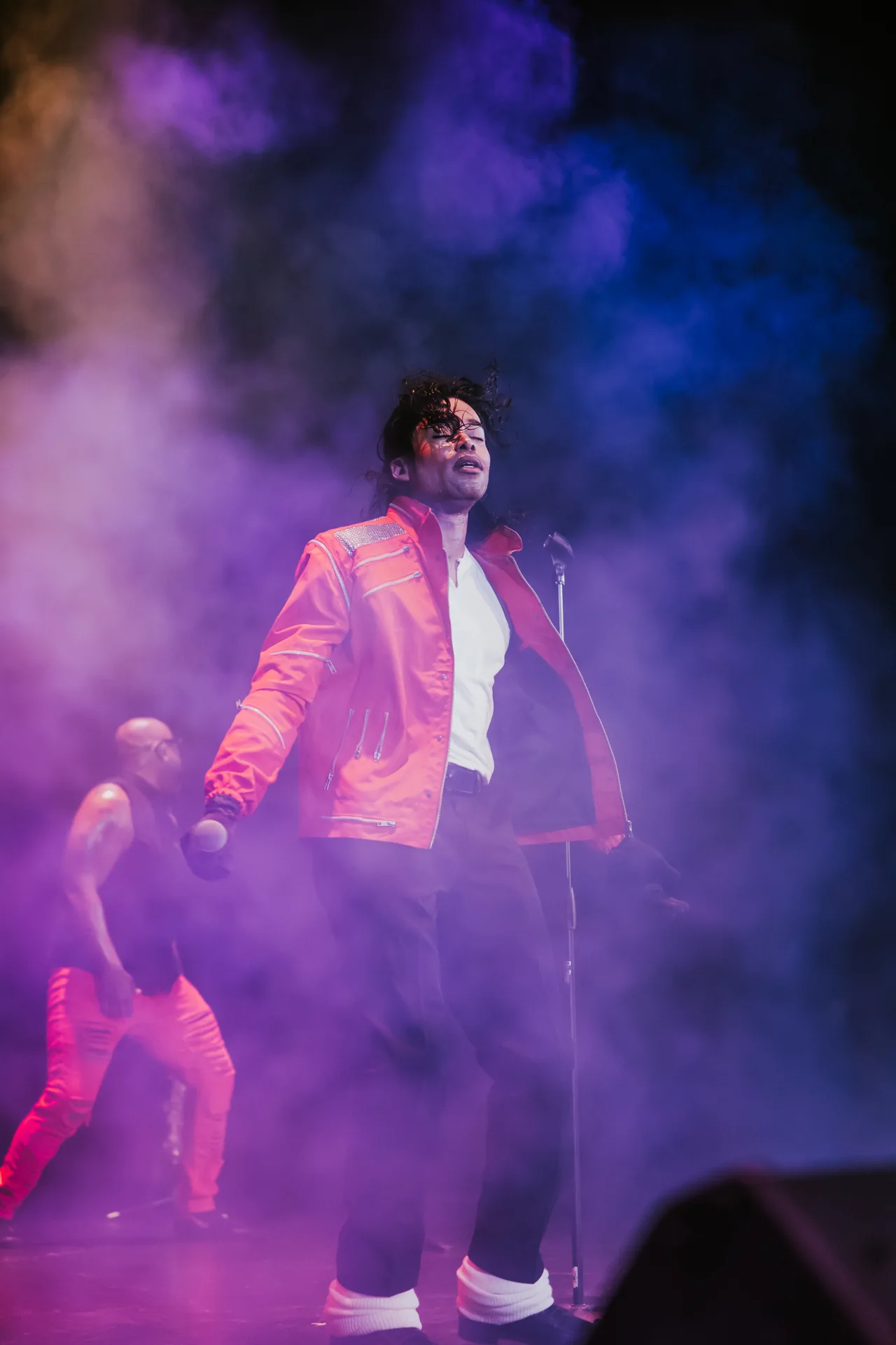 Who’s Bad performer in a red jacket on stage, surrounded by purple concert lighting