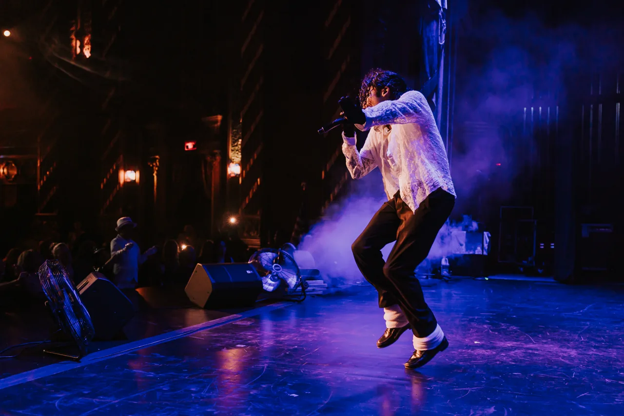 A Who’s Bad performer leaps above the stage in white shirt and fedora, with fans at the front
